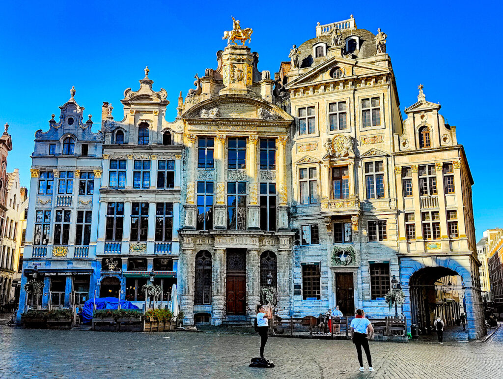 Some of the stunning buildings that line the Grand Place in Brussels with two women standing and taking pictures in the square.