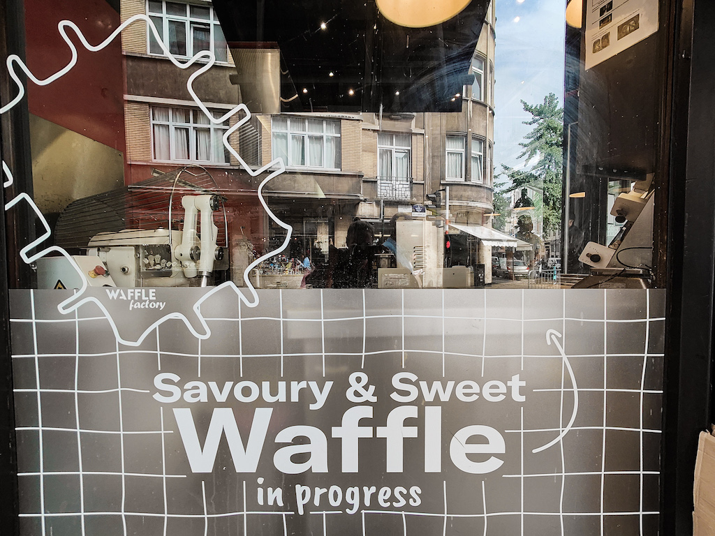 The window on the exterior of Waffle factory iwth white lettering to say they have sweet and savory waffles. 