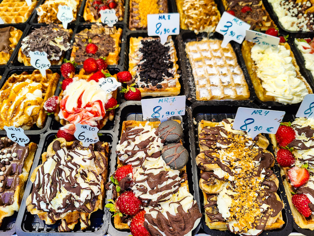 An assortment of Belgian waffles in Brussels covered in sugar, whipped cream, chocolate, strawberries, and more.