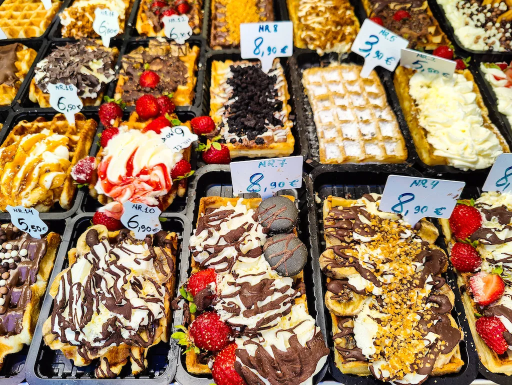 An assortment of Belgian waffles in Brussels covered in sugar, whipped cream, chocolate, strawberries, and more.