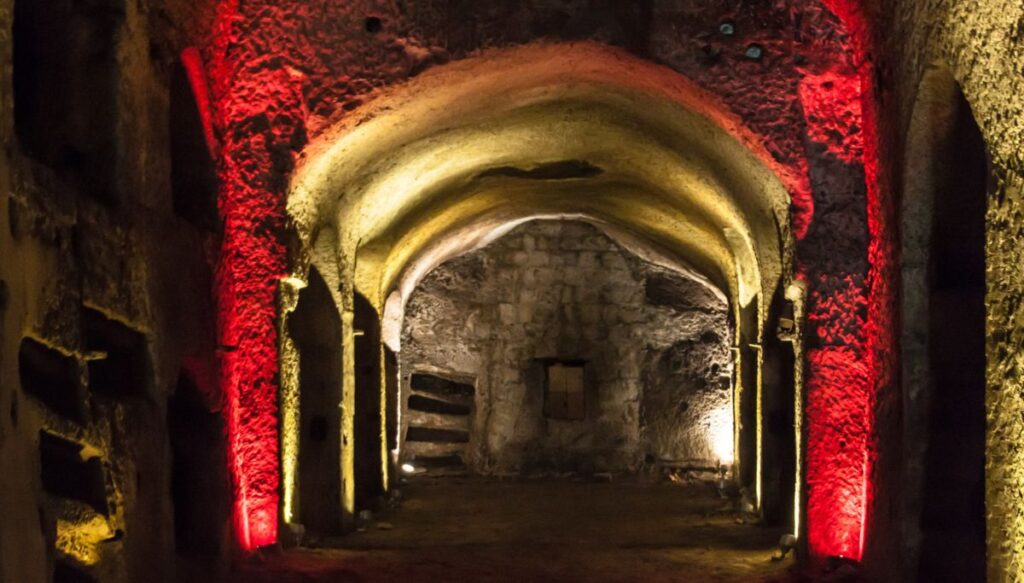 The underground tunnels of the catacombs of san Gennaro all lit-up with yellow and red lights with a central hallway. 