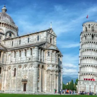 A view of the leaning tower of pisa and the white church sitting next to it as people stand near the bottom taking photos. You can see this and more during one of the best Tuscany wine tours from Florence.