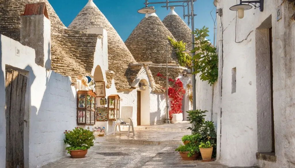 A view down a small street in Puglia that is lined with Trulli. These are white, stone homes with conical roofs and can be seen in Alberobello if you rent a car in Puglia. 