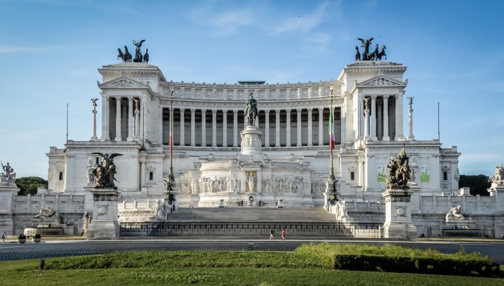 The enormous Altar of the Fatherland structure. it has a giant green stature in the mild and out front while the actual structure is made of white marble columns and topped on eityher side by chariots with horses. 
