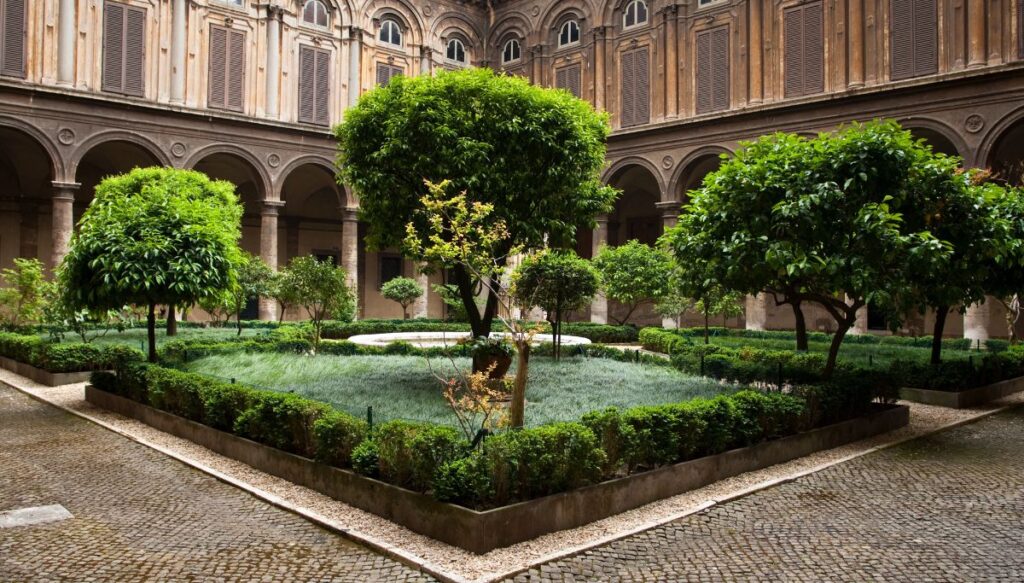 A view of the well manicured garden with trees and bushes that is surrounded by the Doria Pamphilj Gallery in Rome. 