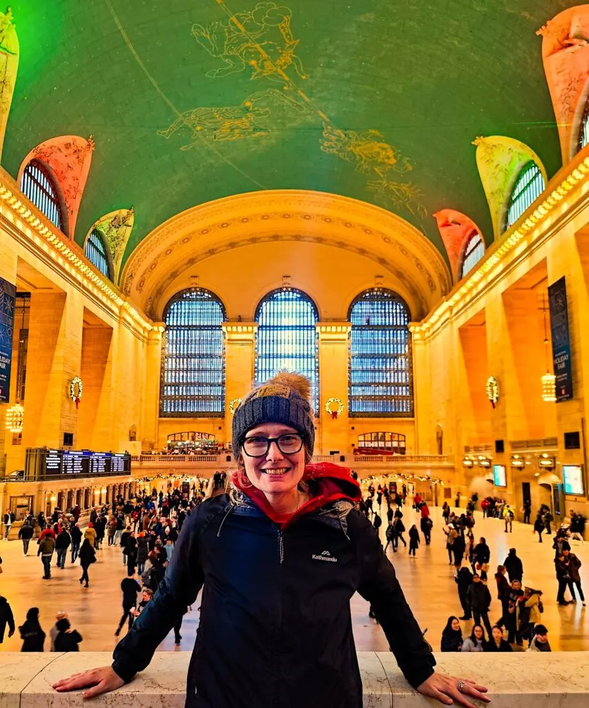 Me standing on the balcony in front of Grand Central Terminal. You can see the red and green Christmas light near the ceiling and the main concourse with its constellation studded ceiling with a turquoise sky.