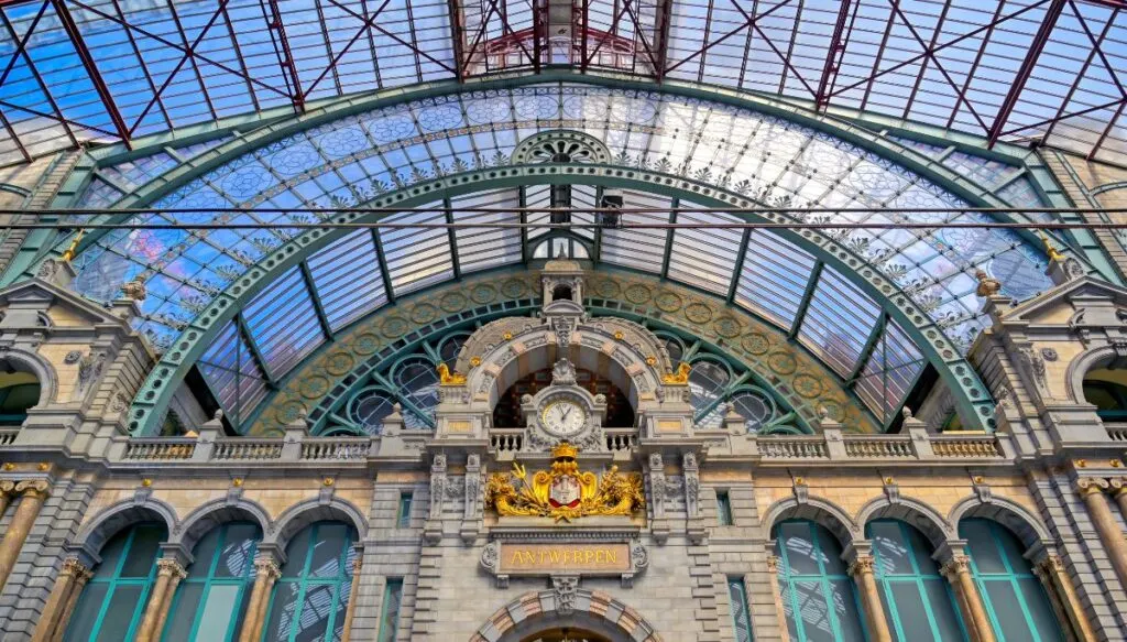 Stunning view of the glass ceiling and ornate gold clock that sit at the center of Antwerp Central Station.