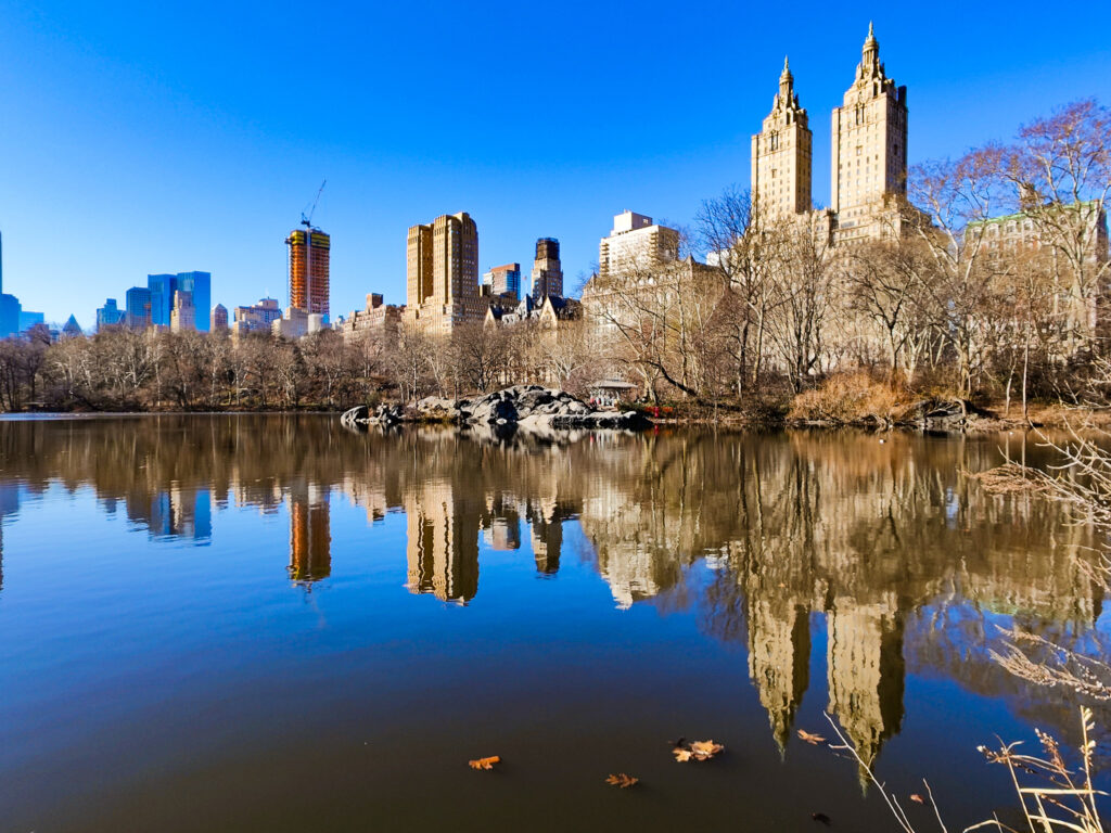 A view of the iconic skyscrapers of the upper west side reflected in the lake in Central Park.