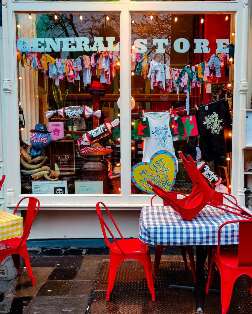 In white letters you see "General Store" inside a window that sells a whole bunch of Cowgirl merch. There are also red chairs and checkered tablecloths on the outside of the restaurant. 