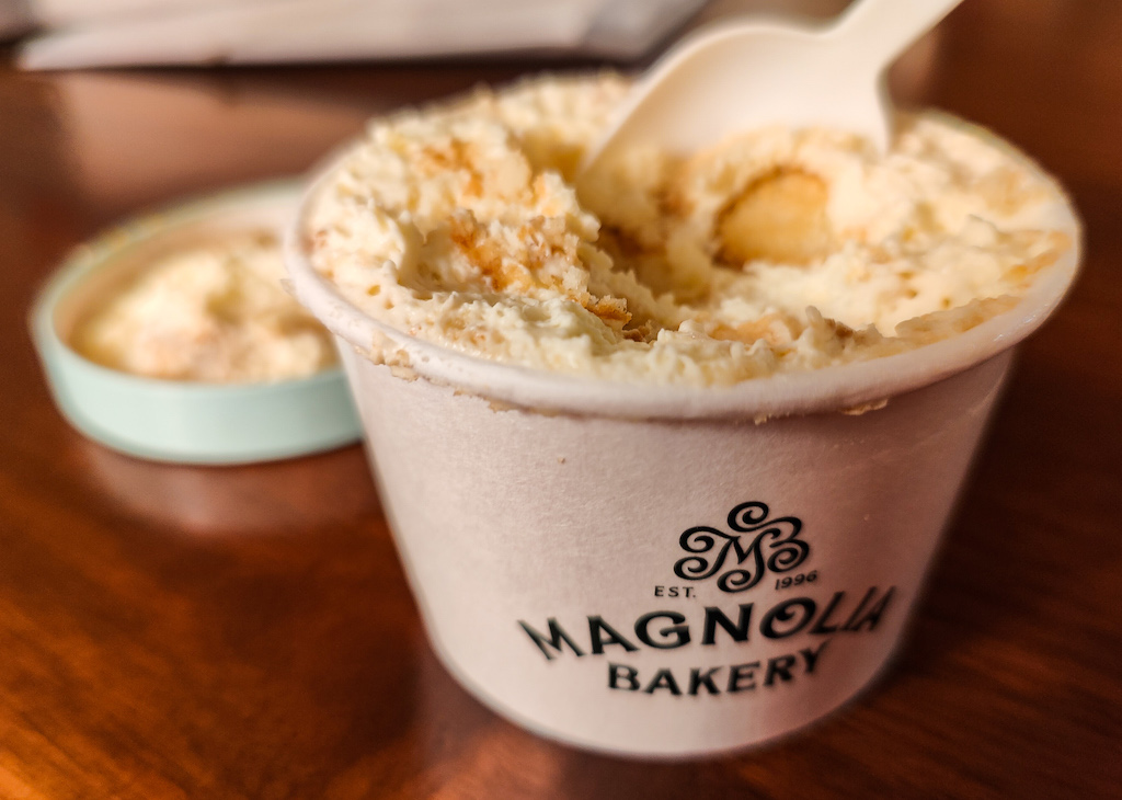 A small container of Magnolia pudding with a white spoon in it. This is one of the best desserts in NYC. 