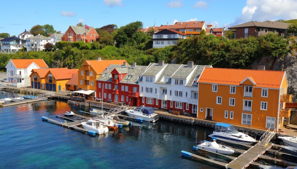 A view of yellow, red and white homes that sit along the water in Haugesund. It is one of the cutest towns in Norway with sailboats in the water. 