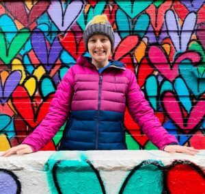 Me standing in front of vibrant grafitti hearts in NYC in a winter coat and a winter har.