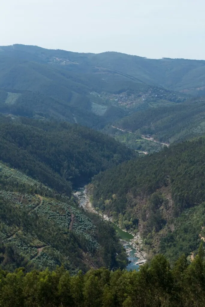 Panoramic view of the green, forested mountains of Arouca Geopark on a sunny day,. You can see a river snaking through the landscape. 