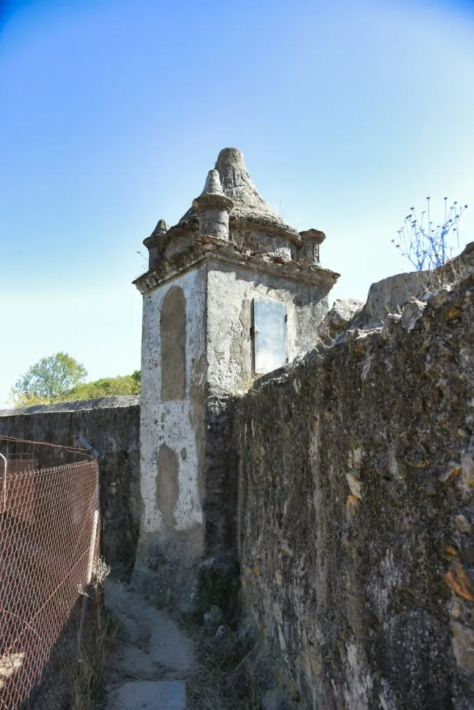 View of an ancient, castle-like tower in Evora on a sunny day. You can see a narrow path with stone walls leading up to the tower. 