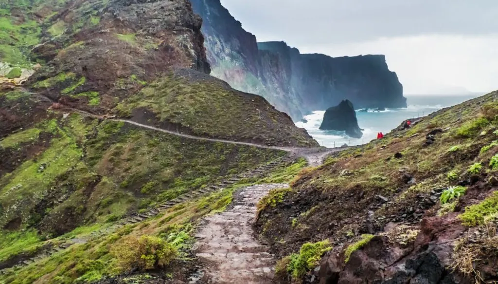 View of the rugged cliffs, beautiful blue waters, stone paths, and green mountains that make up the island of Madeira. 
