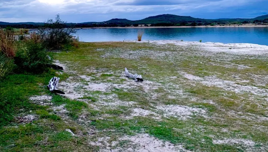 View of the Medina River in Texas. You can see mountaIns behind the river and a sandy shore in front of the river. 