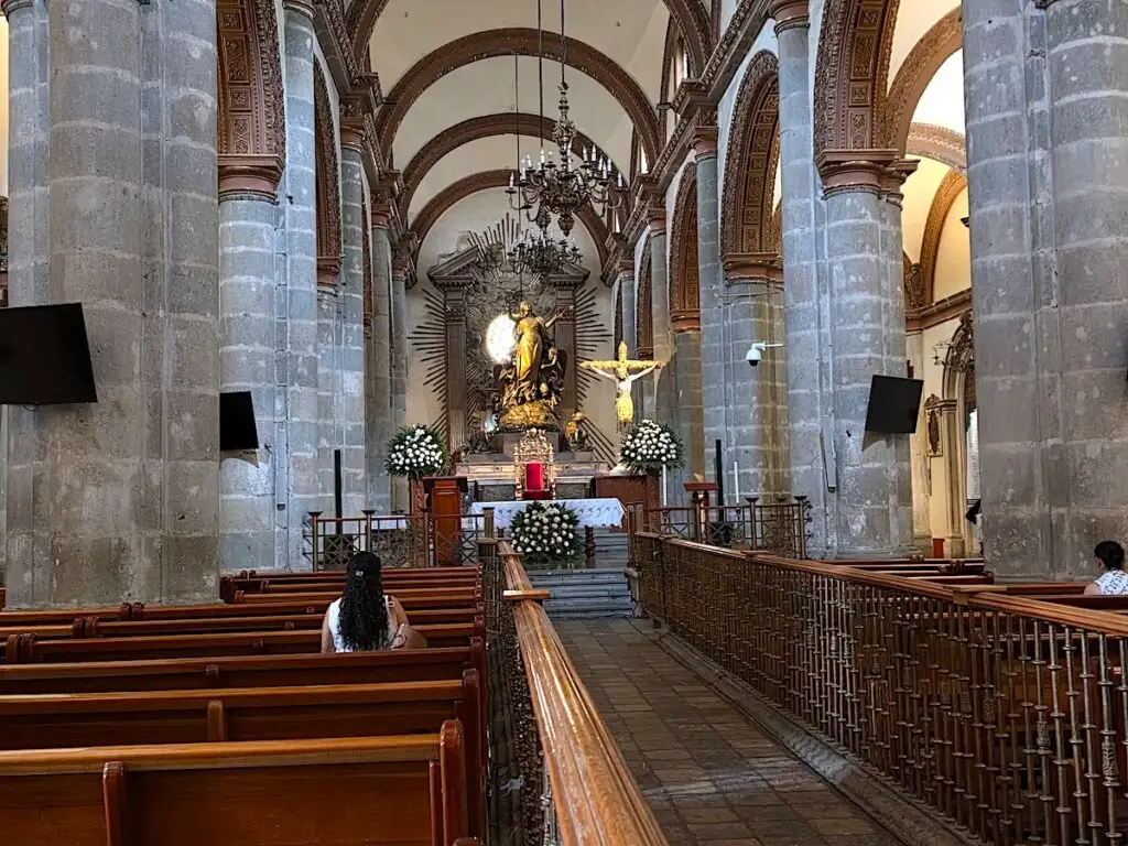 View of the interior of Catedral de Nuestra Se&ntilde;ora de la Asunci&oacute;n. You can see two rows of pews and a central line leading to a statue and altar. 