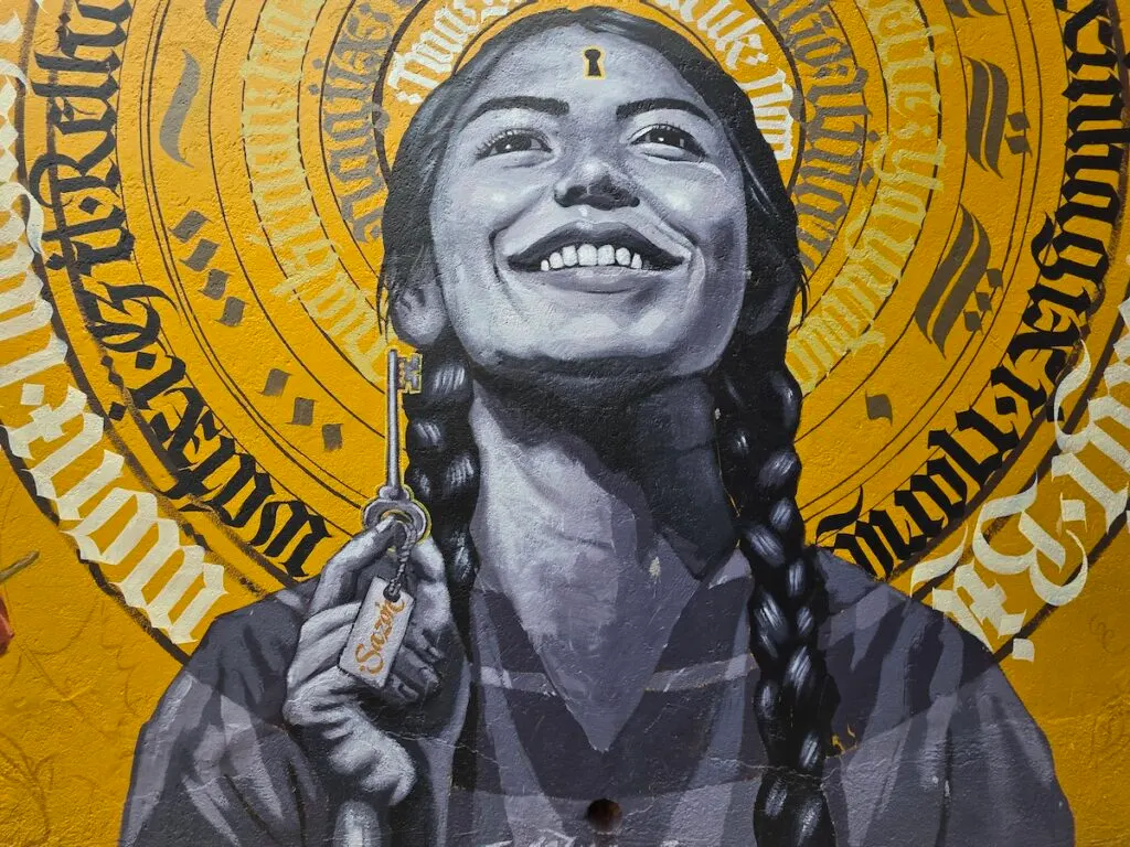 View of a woman in braids holding a key and the outline of the lock is in her head. You can also see yellow behind here with black and white writing in a circle. 