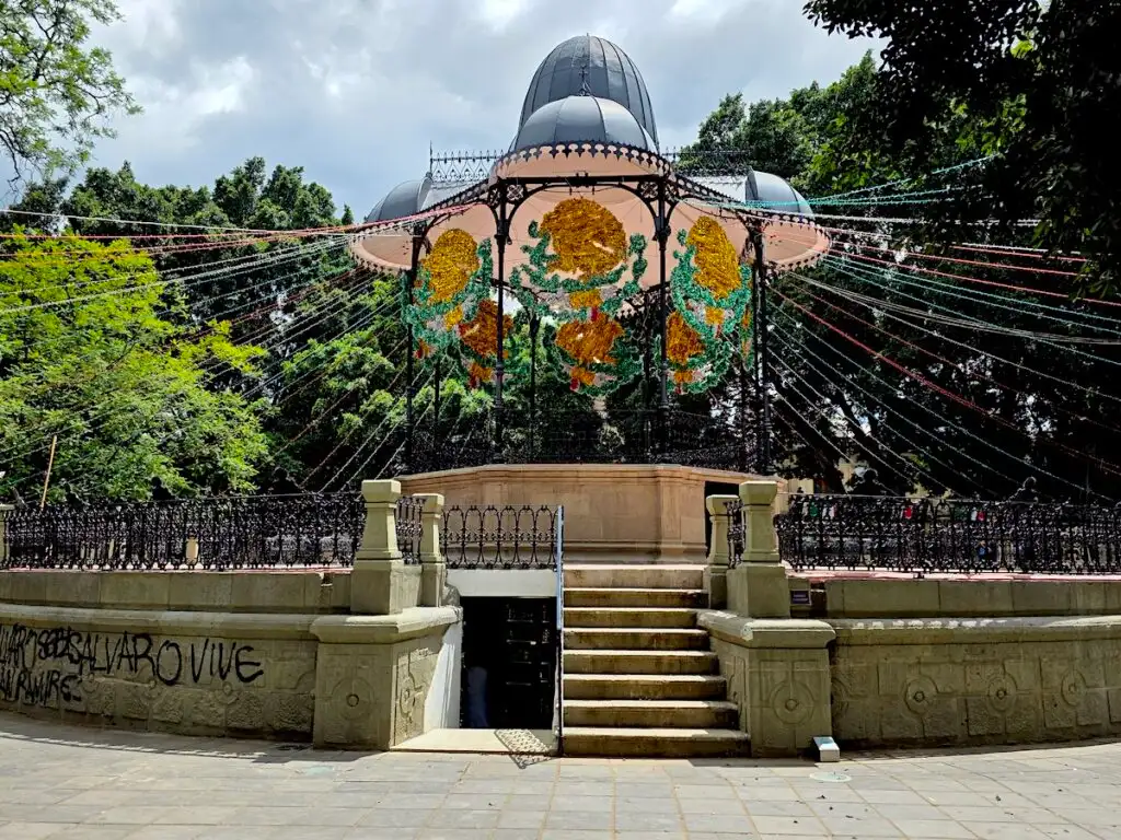 View of an outdoor pavilion in the Zocalo in Oaxaca. You can see decorations on the pavillion. 