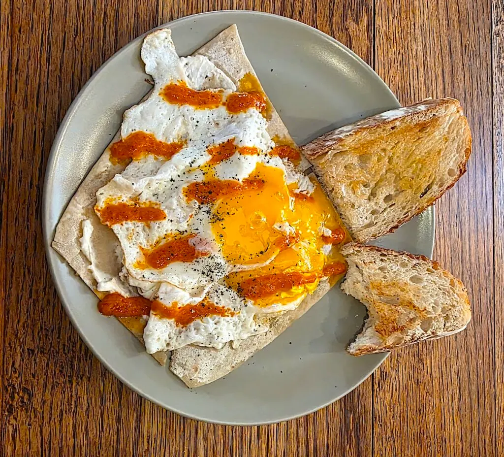 Aerial view of my Turkish eggs with red sauce and on tortillas. On the right you can see sourdough bread with butter. 