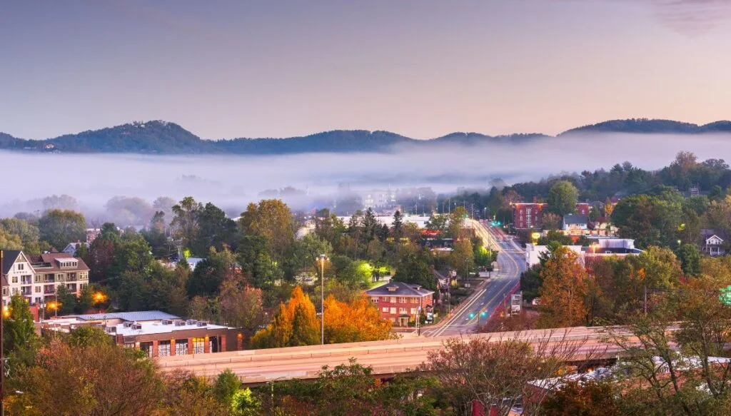 Aerial view of the historic homes and brick buildings in Asheville. You can see mist hanging below the mountains in the background. 