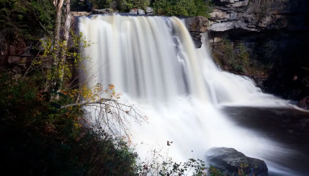 View of a giant waterfall in Blackwater Falls State Park that is surrounded by vibrant fall foliga. 