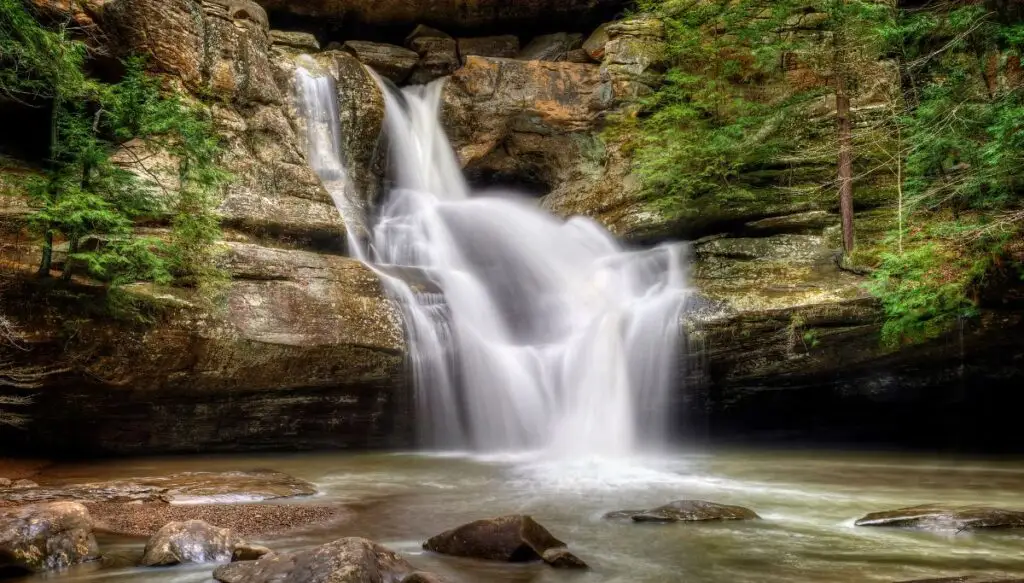 View of Cedar Falls going down the edge of a rock face with trees all around the edge of the waterfall. 