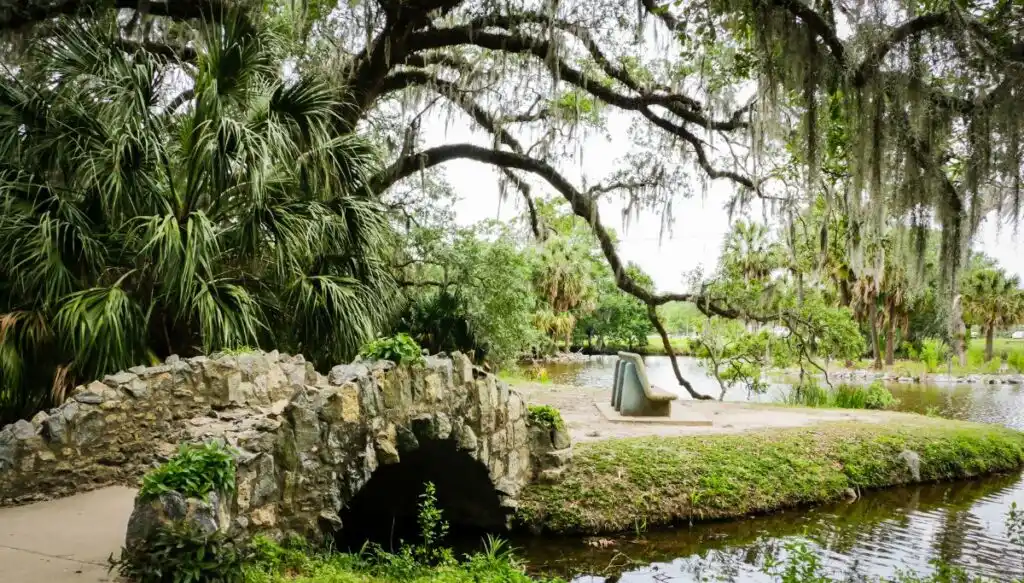 View of a stone bridge going over a stream beneath a oak tree with Spanish Moss on it. 