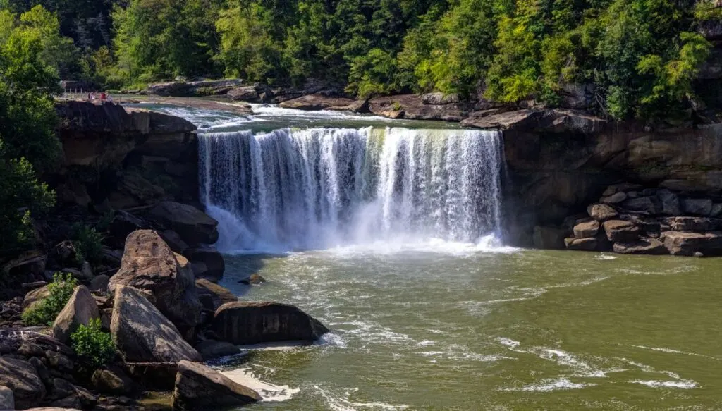 Aerial view of Cumberland Falls falling into the river below with the river being surrounded by lush green trees. 