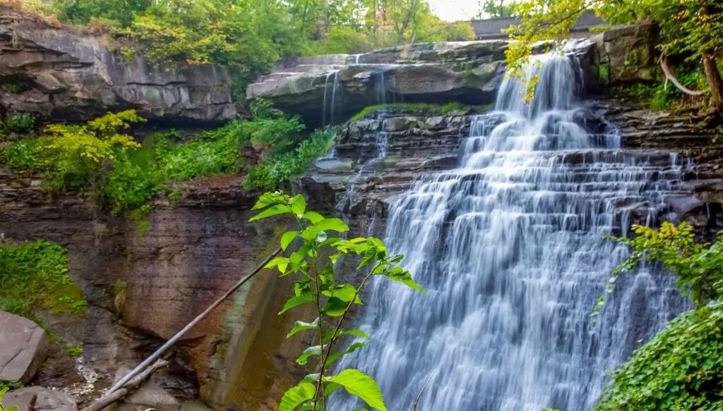View of a sheer rock face with a wtaerfall running down it that is surrounded by lush green plants in Cuyahoga Valley National Park. 