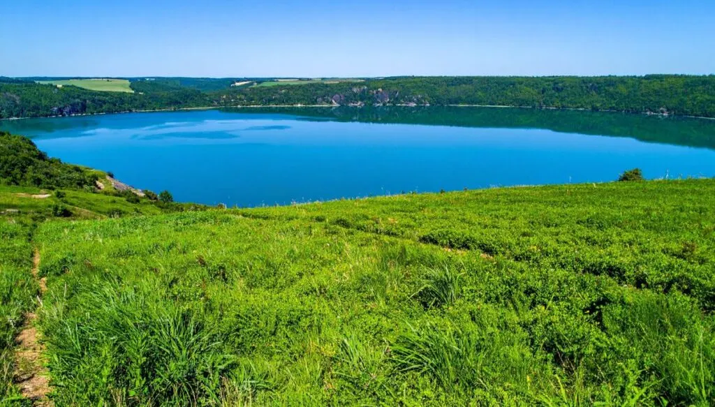 Aerial view of a Devil's Lake that is surrounded by lush grass and lots of trees on a sunny day. 