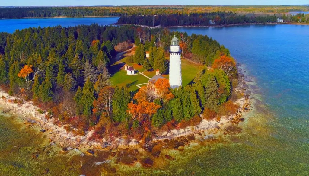 View of a small island with lots of pine trees and w hite lightouse with some trees changin color in autumn. 