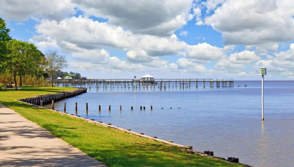 View of paths along the grass lined shores of the Ocean. You can also see piers jutting out into the water in the distance on a clear and sunny day. 
