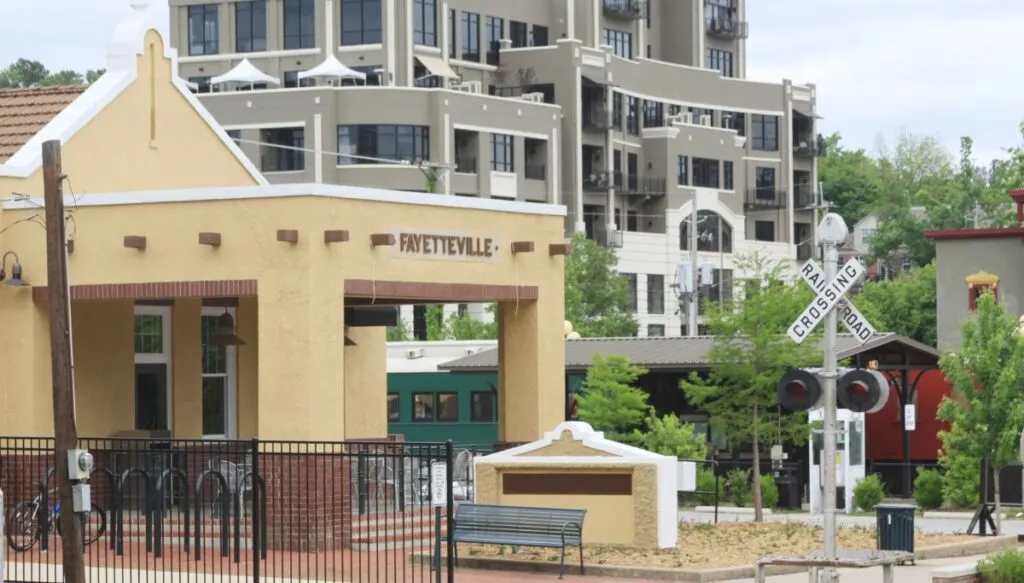 View of the beige/yellow colored historic train station with a railroad crossing sign in Fayetteville, Arkansas. 