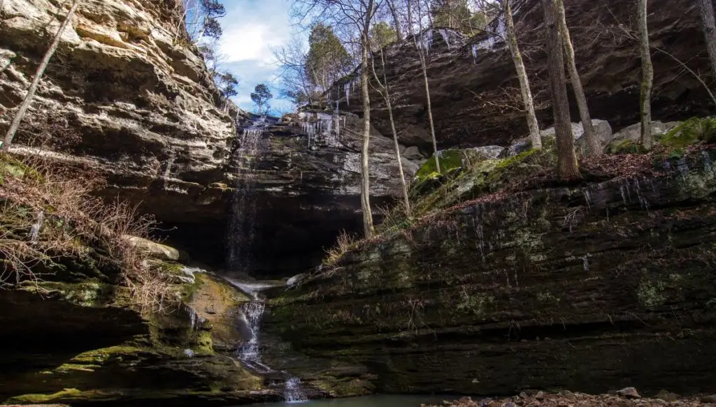 View of a waterfall cascading down a rocky cliff with various rock ledges with trees goring on them in  Ferne Clyffe State Park