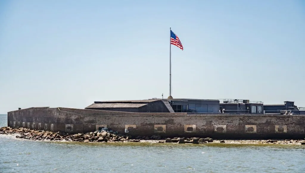 View of Fort Sumter National Monument sitting in the water. You can see the flag waving in the American breeze and the fort around the flag. 