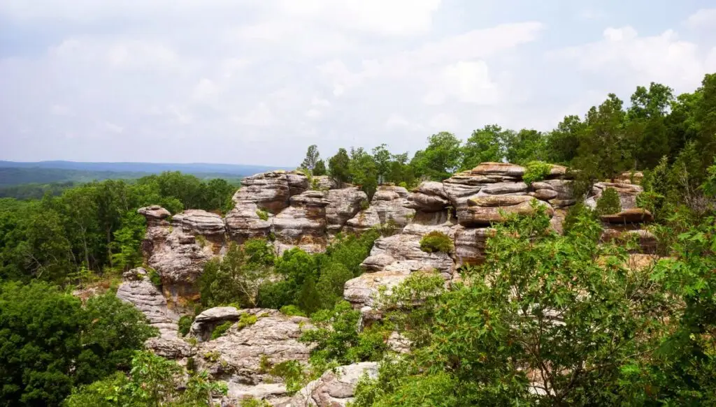 View of unique rock formations surrounded by leafy green trees inside of Garden of the Gods in Shawnee National Forest. 