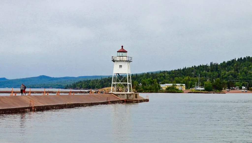 View of a small white lighthouse sitting out on the water in Grand Marais. 
