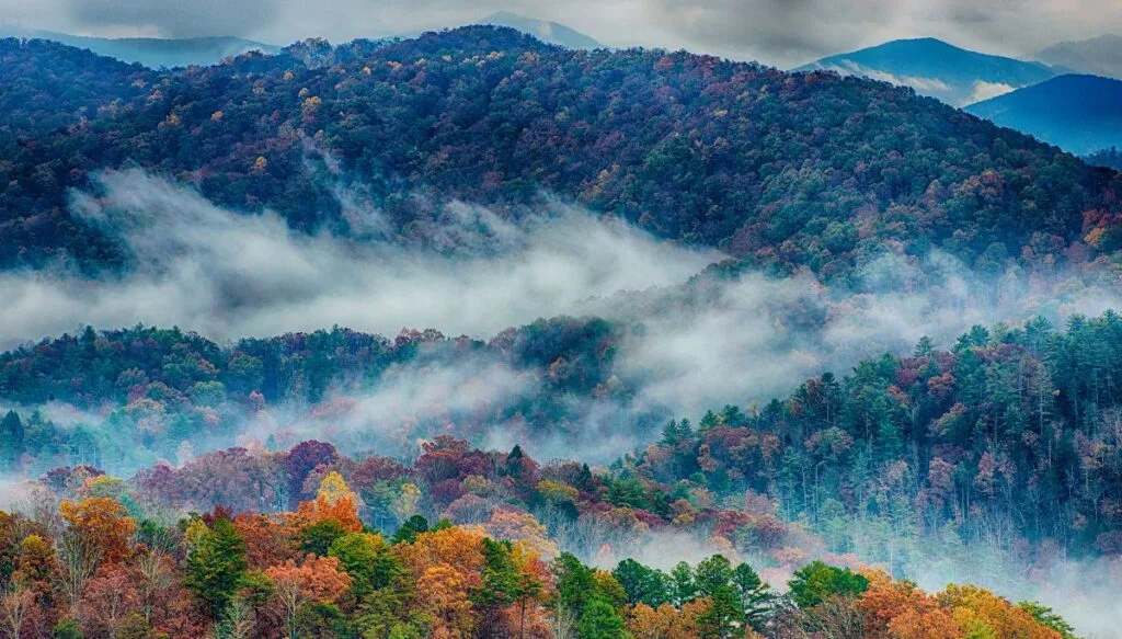 View of mountains filled with fall foliage with mist hanging over the mountains in Great Smoky Mountains National Park. 