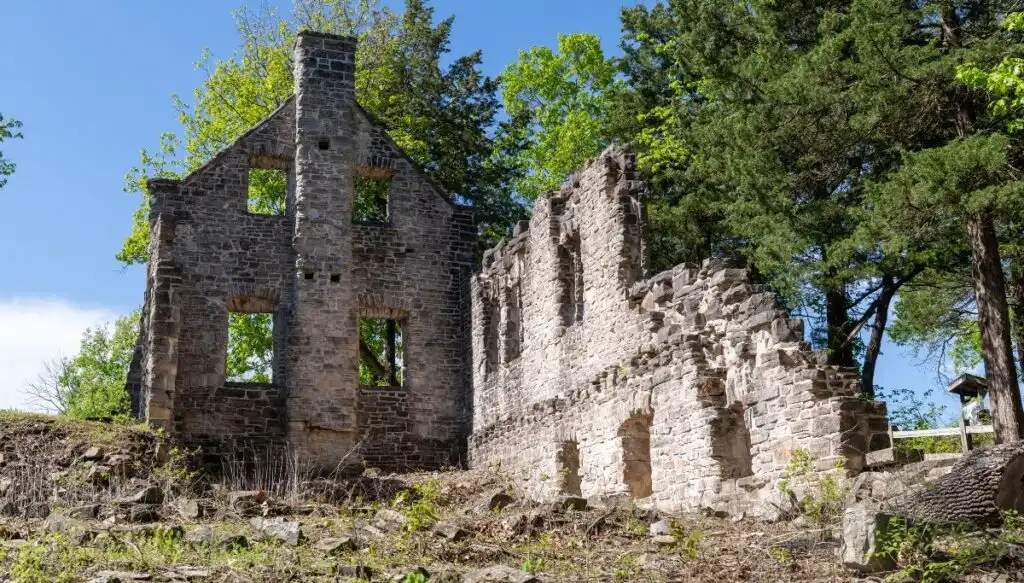 View of old castle ruins inside of Ha Ha Tonka State Park in Missouri. You can see the old stone ruins of a house that is surrounded  by leafy green trees. 