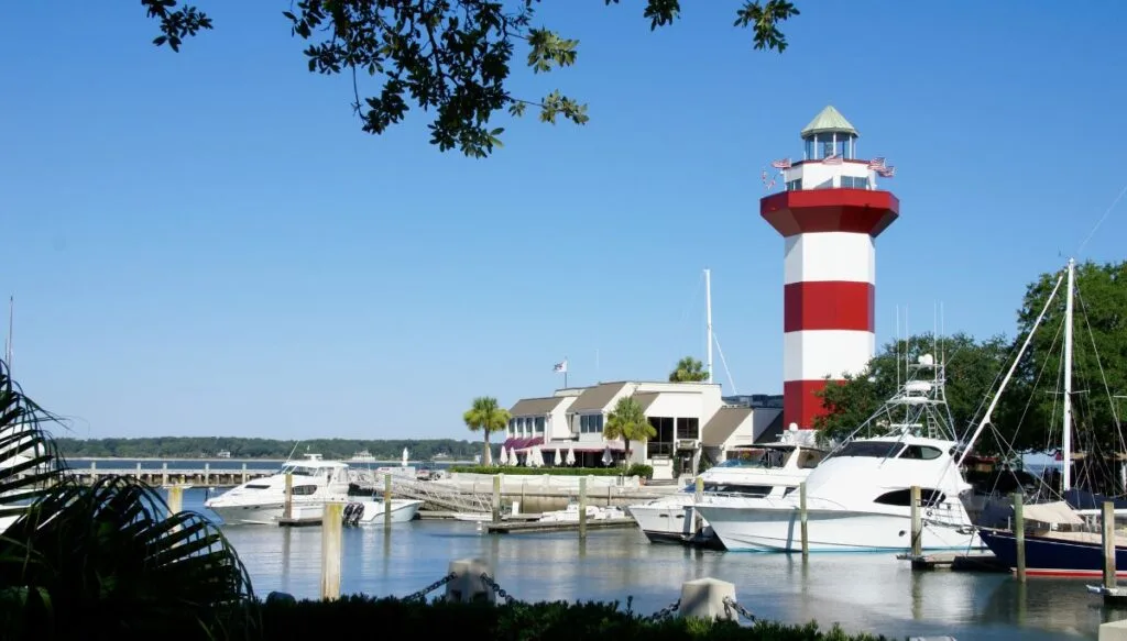 View of the harbor with boats in the water and a lighthouse standing tall with red and white stripes. 