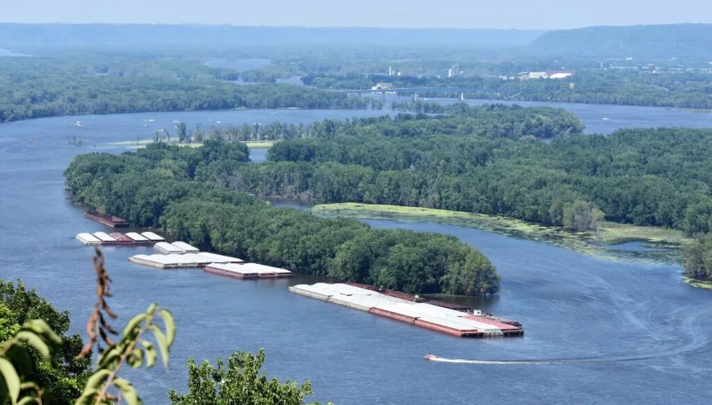 View of containers and boats in the river. Youy can see an aerial view of the river and many green islands from River Bluffs Scenic Byway. 