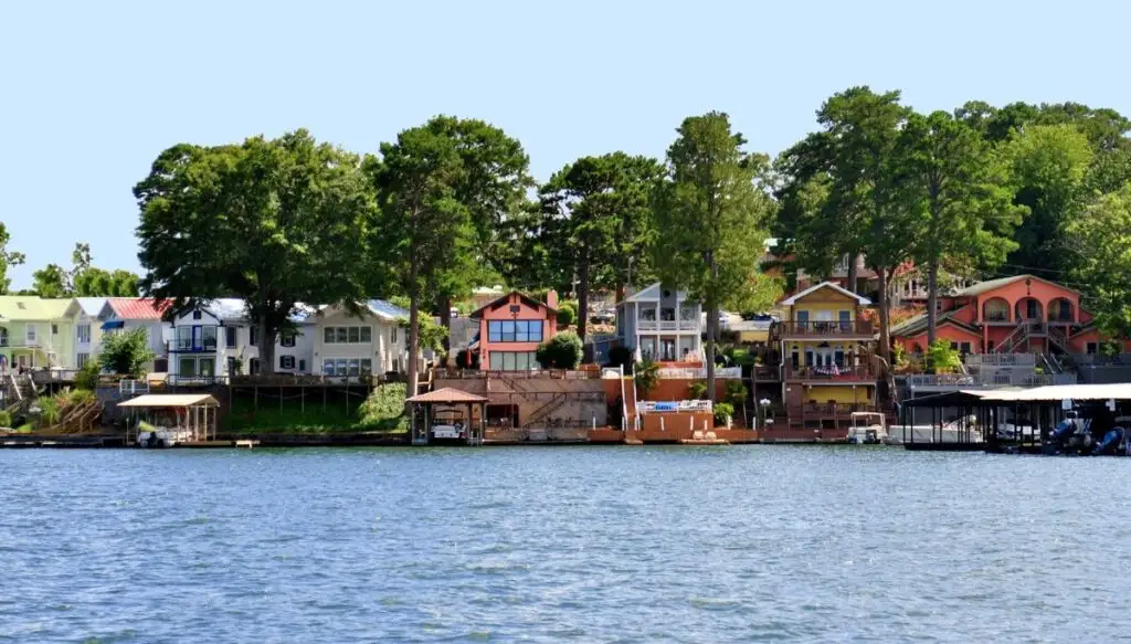 View of an assortment of colorful homes sitting along the edge of Lake Hamilton in Arkansas. You can also see tall leafy trees in the background. 
