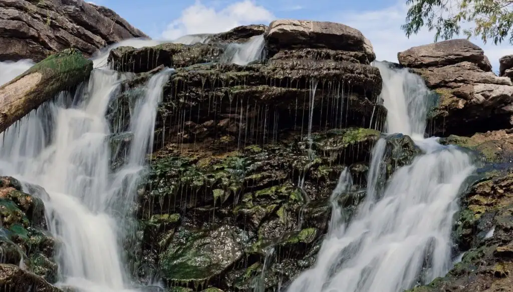 View of a waterfalls spilling over moss covered stones inside of Lake Macbride State Park. 