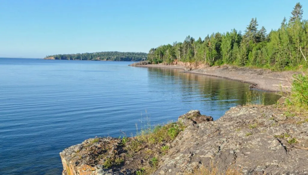 View of rocks and pine trees sitting along the North Shore of Lake Superior on a sunny day. 