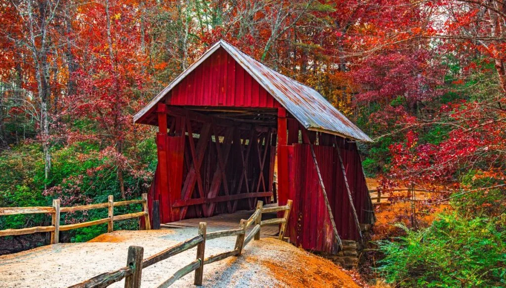 View of a red covered bridge with fall foliage all around it in Landrum. 