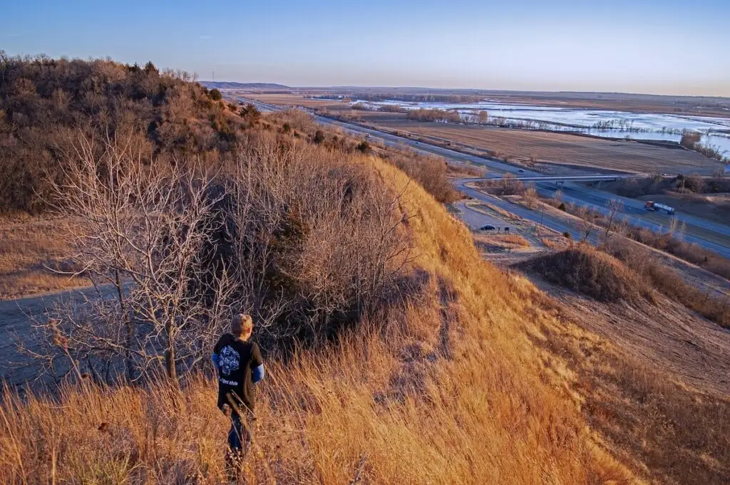 View of a man in black walking along the top of the Loess Hills with the river off in the distance on the left. 