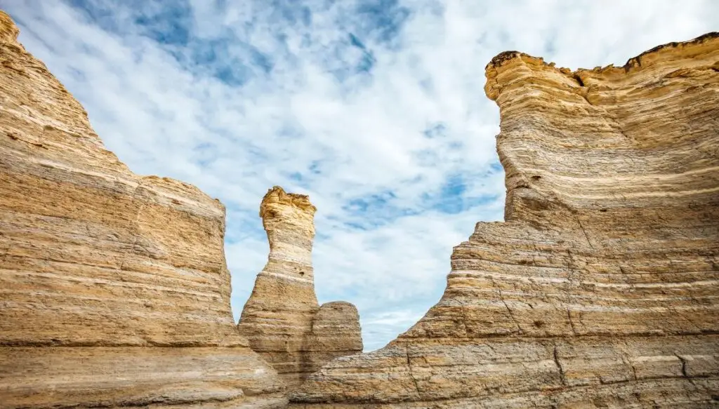 View of the white rock formations at Monument Rocks in Kansas. You can see horizontal stripes in the rocks which are set against a blue sky with clouds. 