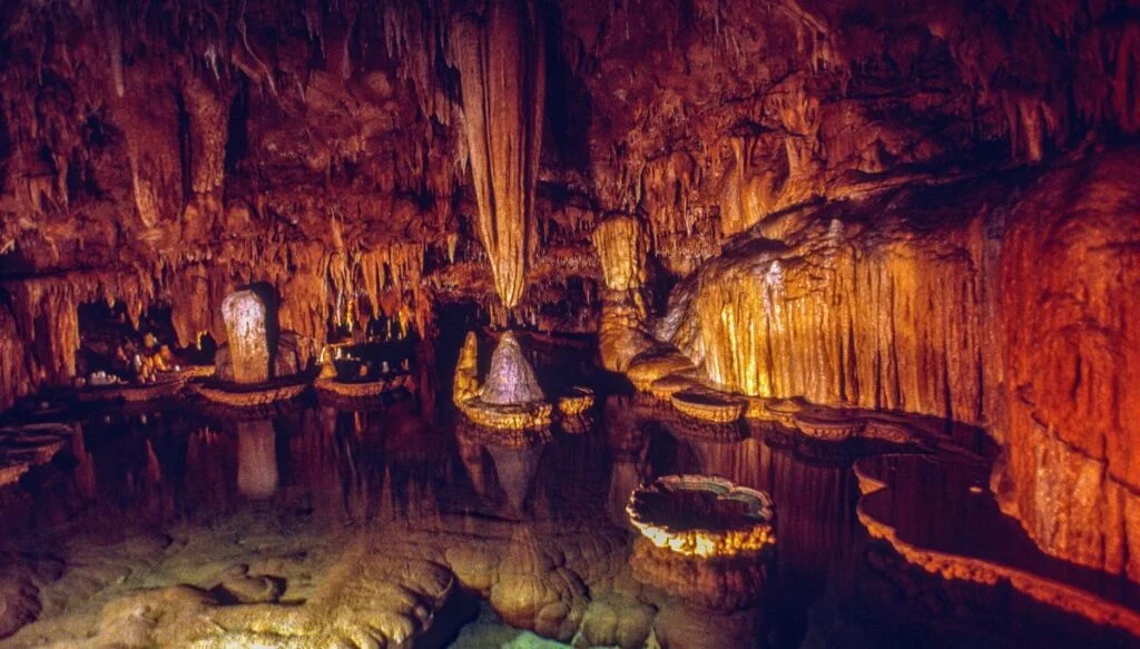 View of rock formations hanging from the ceiling and water on the ground inside of Onondaga Cave State Park, 
