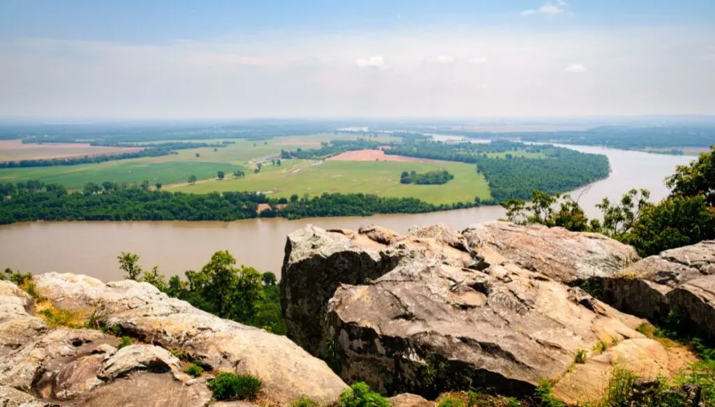 Aerial view from a series of rocks sitting above a vast river in Petit Jean State Park. You can also see vast fields in the background the stretch out along the edge of the river. 